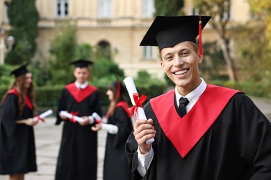 Photo of Happy students with diplomas after graduation ceremony outdoors, selective focus