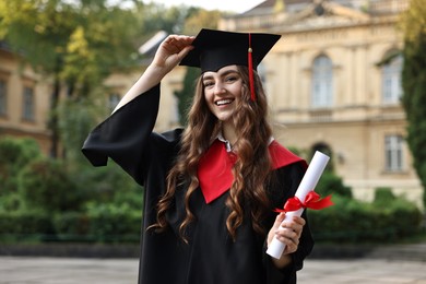 Photo of Happy student with diploma after graduation ceremony outdoors