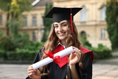 Photo of Happy student with diploma after graduation ceremony outdoors