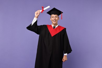 Happy student with diploma after graduation on violet background