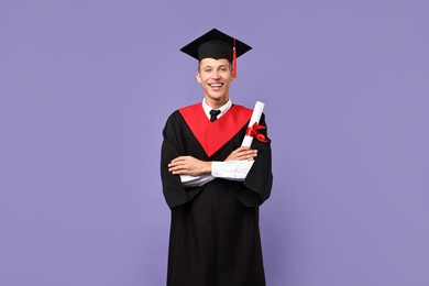 Happy student with diploma after graduation on violet background