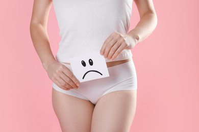 STD (sexually transmitted disease). Woman holding sticky note with drawn sad face on pink background, closeup