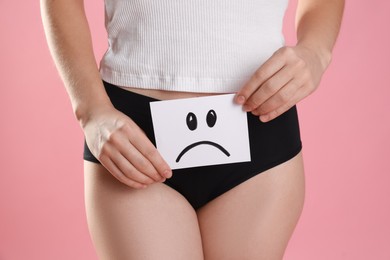 STD (sexually transmitted disease). Woman holding sticky note with drawn sad face on pink background, closeup