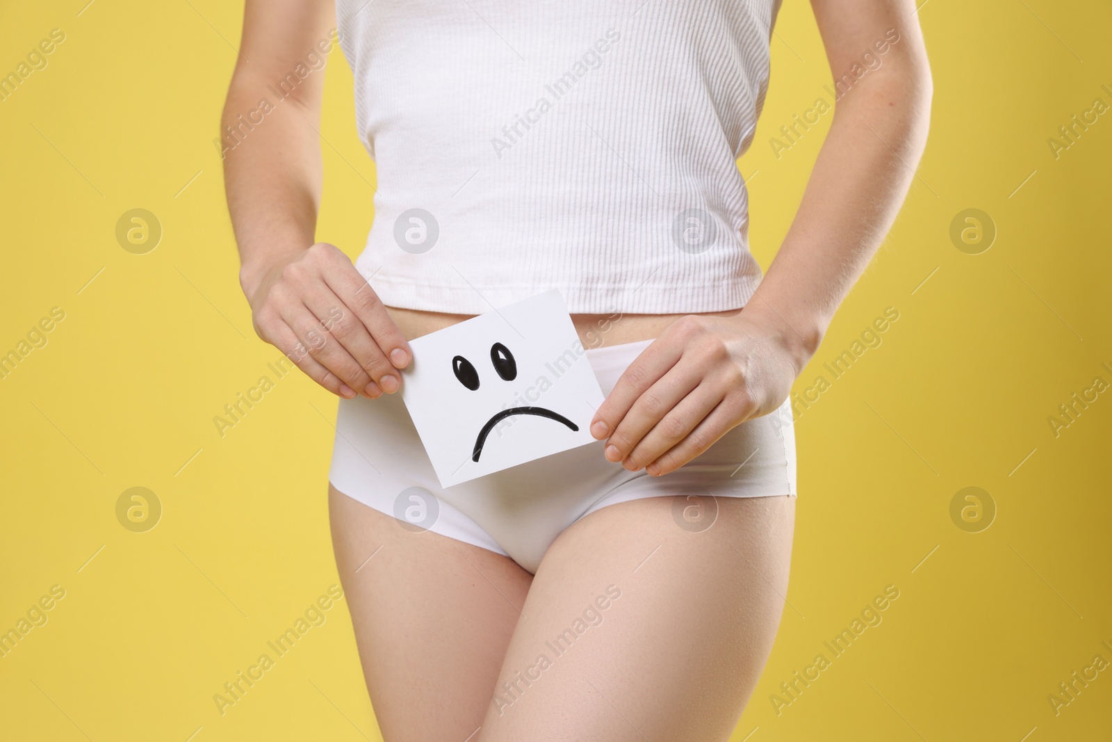 Photo of STD (sexually transmitted disease). Woman holding sticky note with drawn sad face on yellow background, closeup