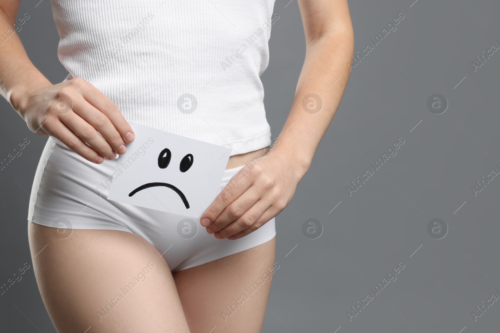 Photo of STD (sexually transmitted disease). Woman holding sticky note with drawn sad face on grey background, closeup. Space for text