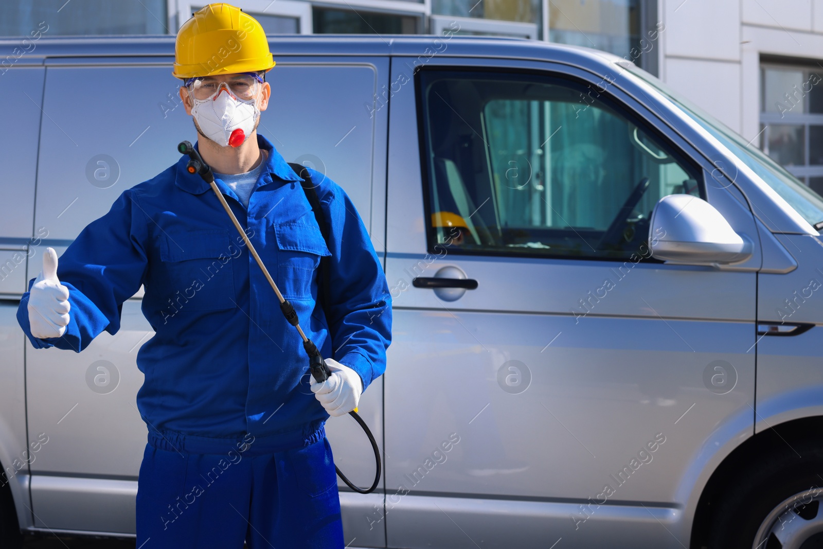 Photo of Pest control worker with spray tank showing thumbs up outdoors