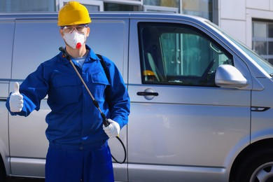 Photo of Pest control worker with spray tank showing thumbs up outdoors