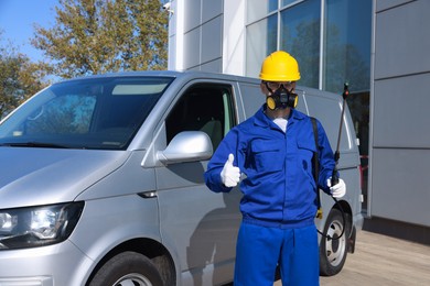 Photo of Pest control worker with spray tank showing thumbs up outdoors