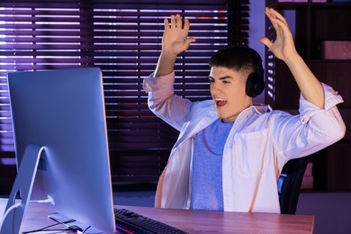 Photo of Emotional young man playing video game with keyboard at wooden table indoors