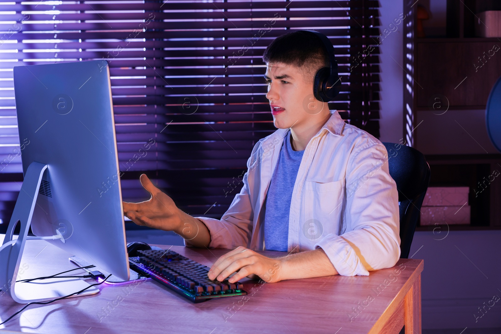 Photo of Young man playing video game with keyboard at wooden table indoors