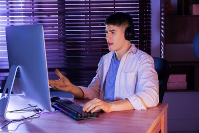 Photo of Young man playing video game with keyboard at wooden table indoors