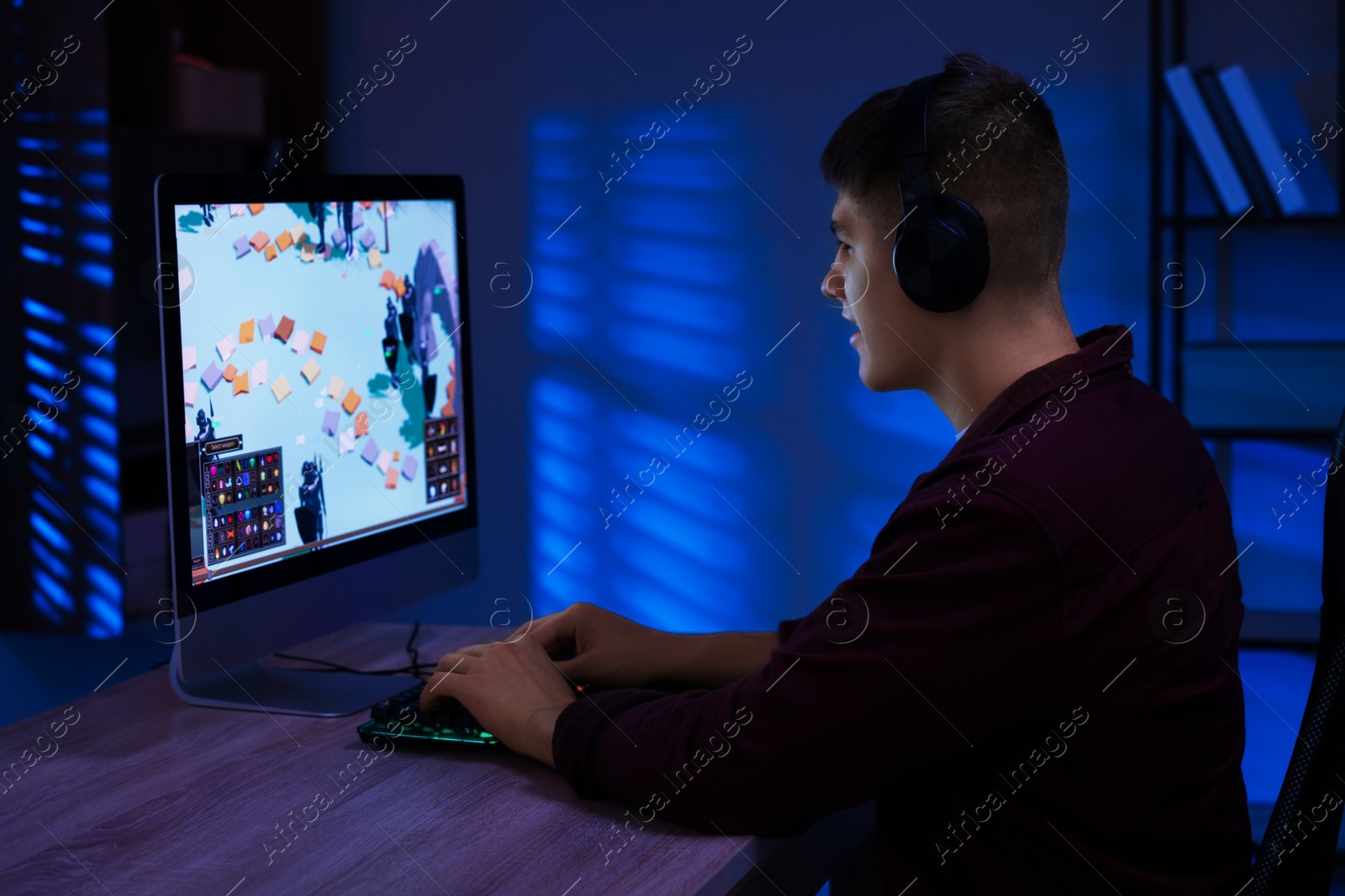 Photo of Young man playing video game with keyboard at wooden table indoors