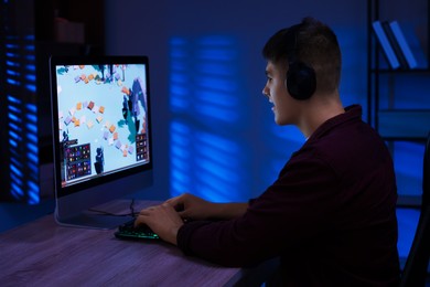 Photo of Young man playing video game with keyboard at wooden table indoors