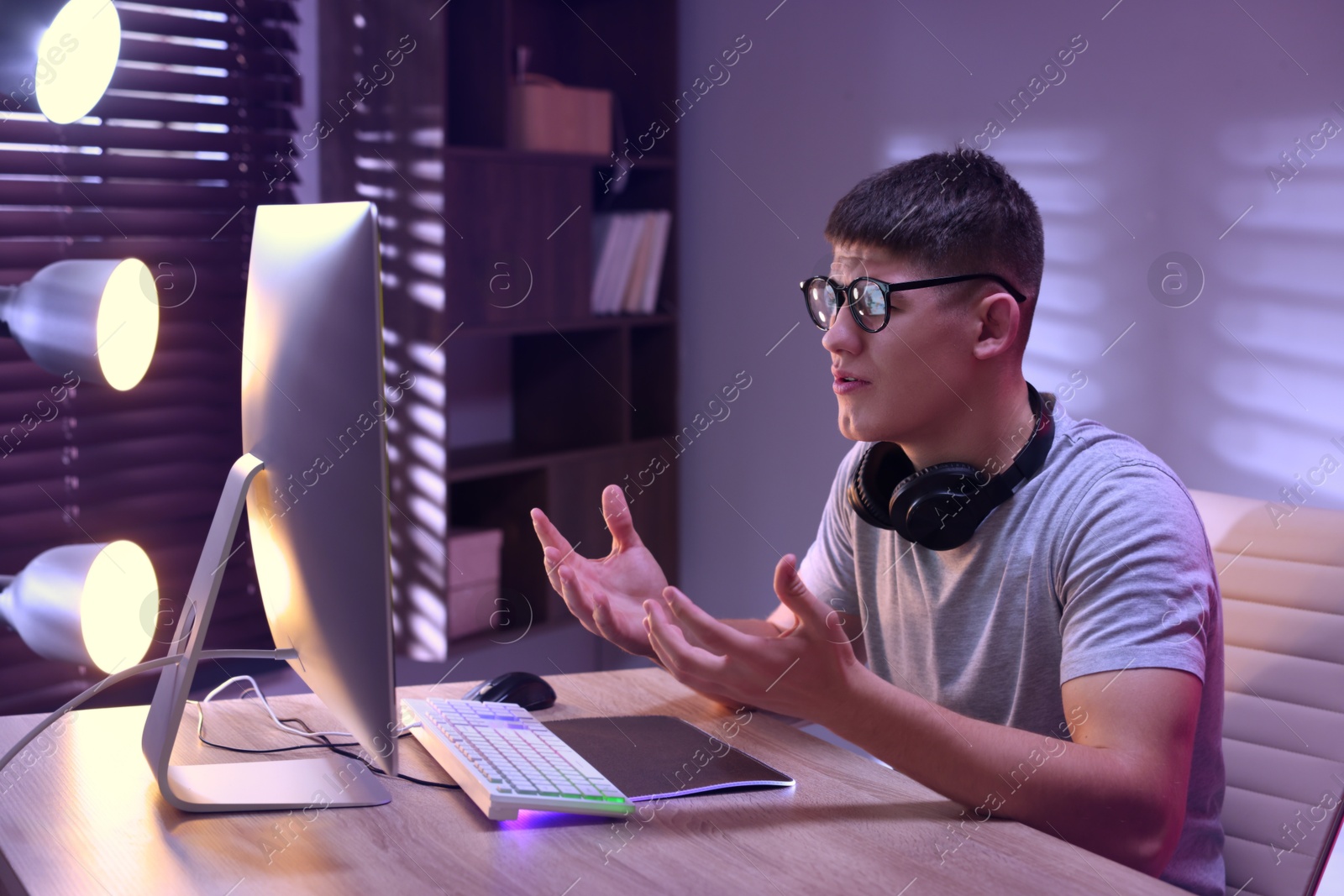 Photo of Emotional young man playing video game with keyboard at wooden table indoors