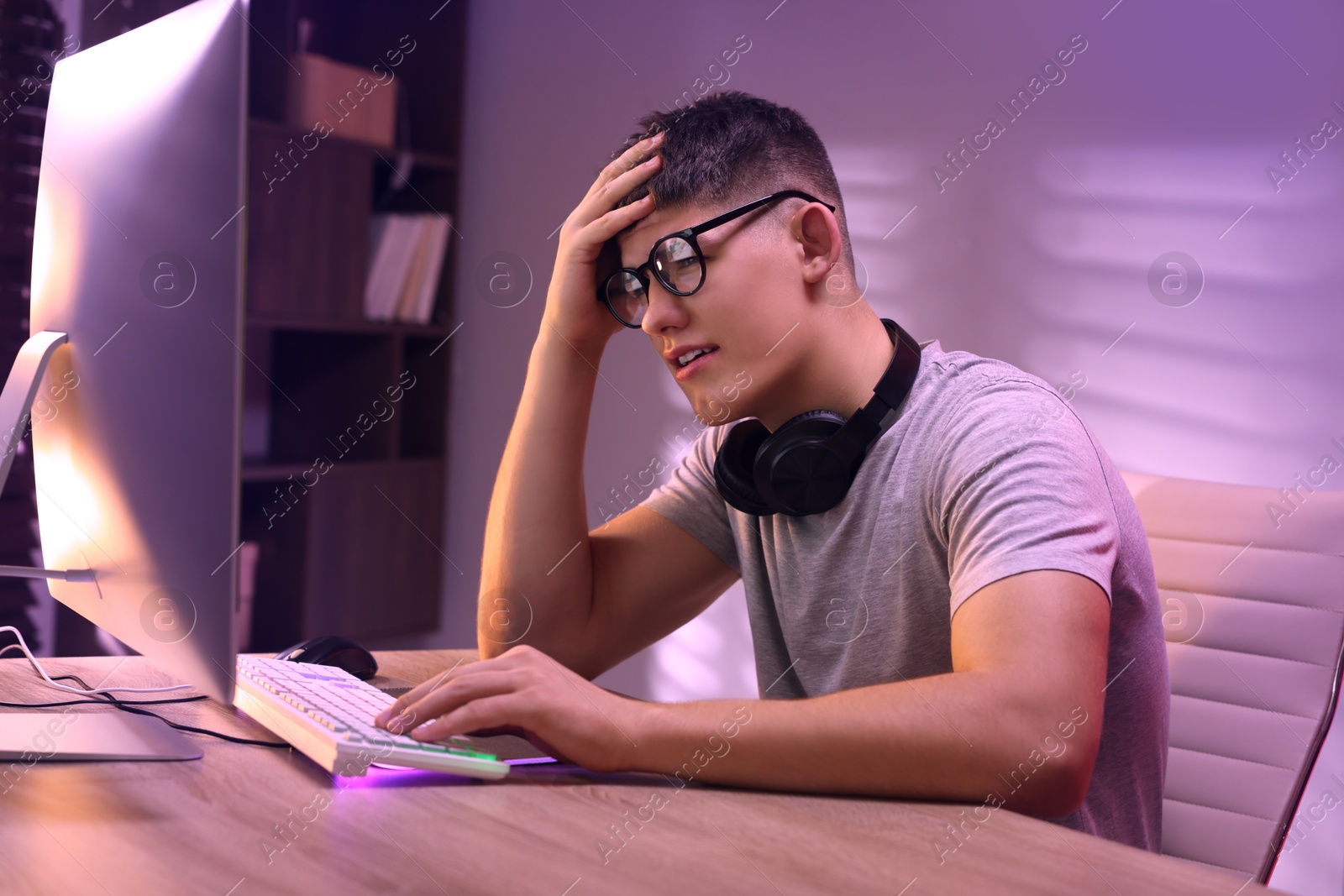 Photo of Young man playing video game with keyboard at wooden table indoors