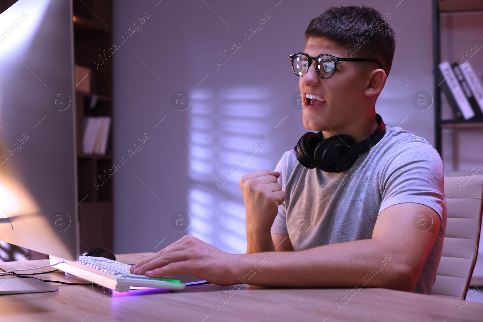 Photo of Young man playing video game with keyboard at wooden table indoors