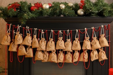 Photo of Christmas advent calendar with gifts and decor hanging on fireplace indoors