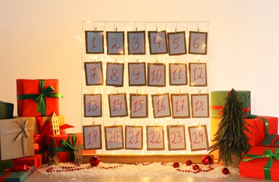 Photo of Handmade advent calendar, gifts and decor on table near light wall. Christmas tradition