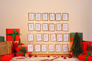 Photo of Handmade advent calendar, gifts and decor on table near light wall. Christmas tradition