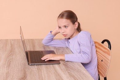 Photo of Girl with incorrect posture using laptop at wooden desk on beige background