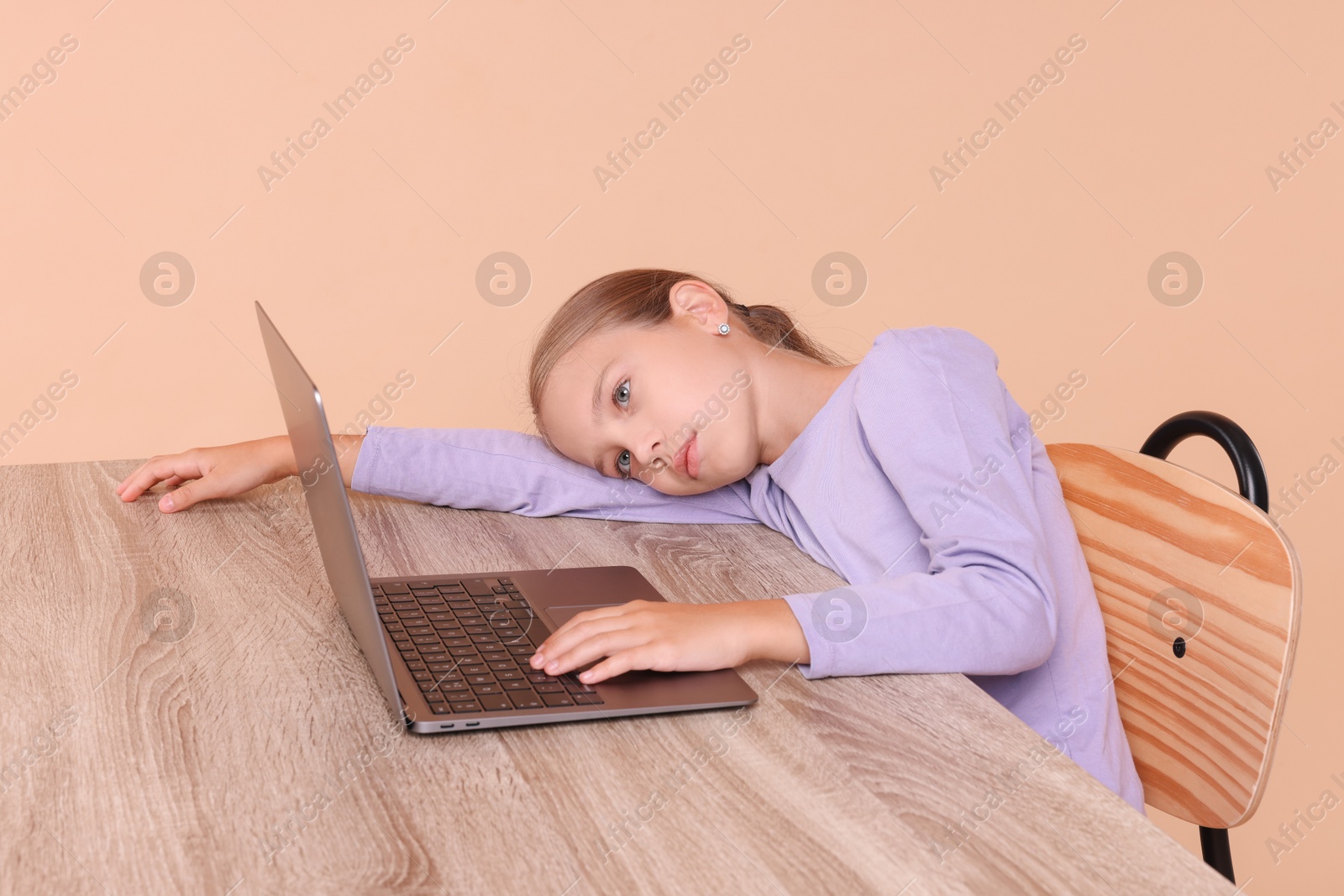 Photo of Girl with incorrect posture using laptop at wooden desk on beige background