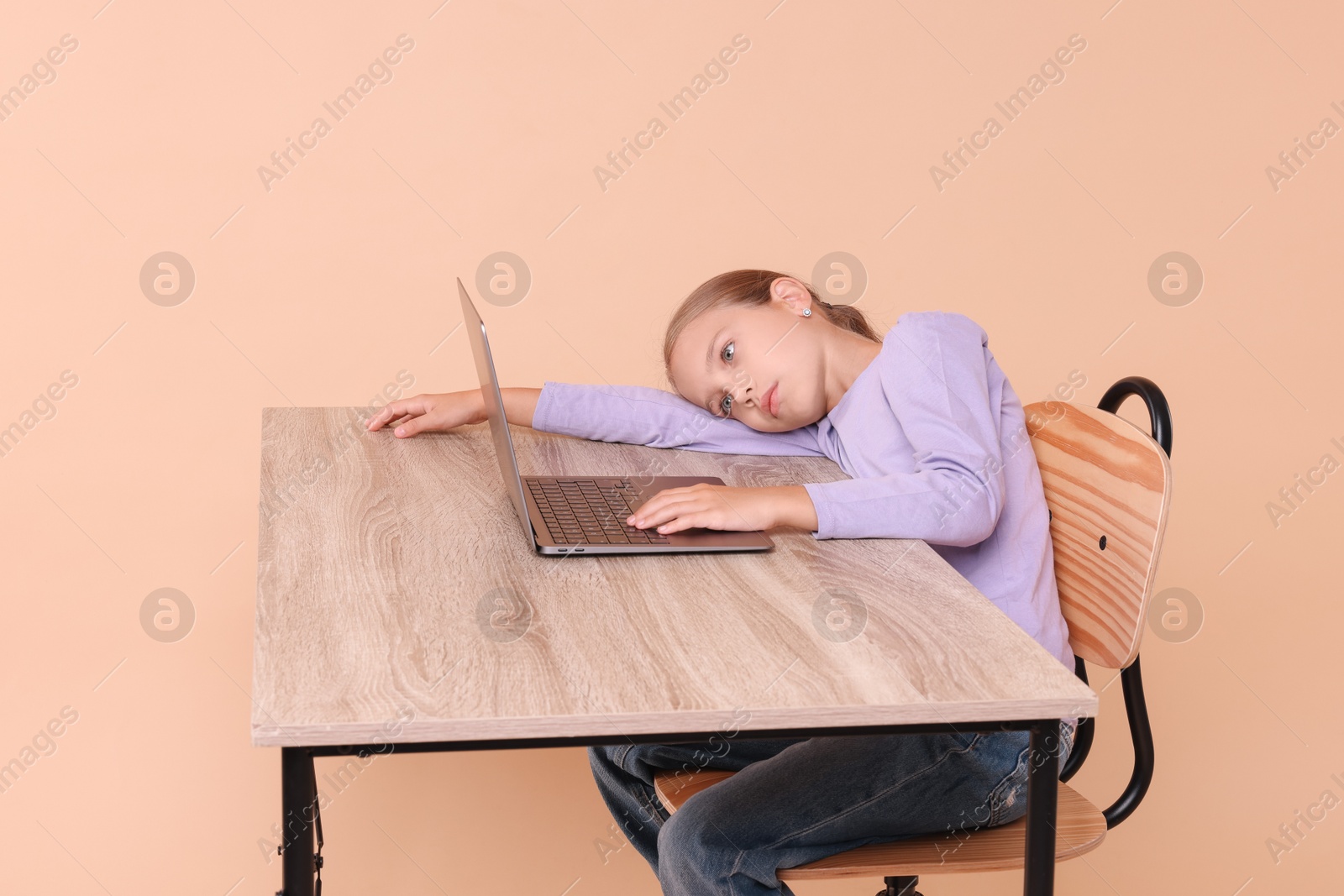 Photo of Girl with incorrect posture using laptop at wooden desk on beige background