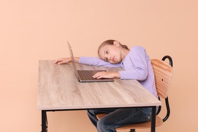 Girl with incorrect posture using laptop at wooden desk on beige background