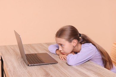 Photo of Girl with incorrect posture using laptop at wooden desk on beige background