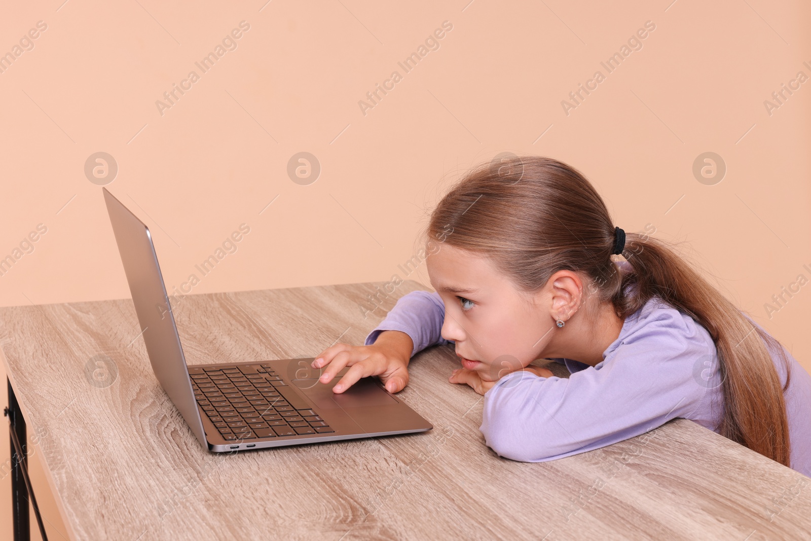 Photo of Girl with incorrect posture using laptop at wooden desk on beige background