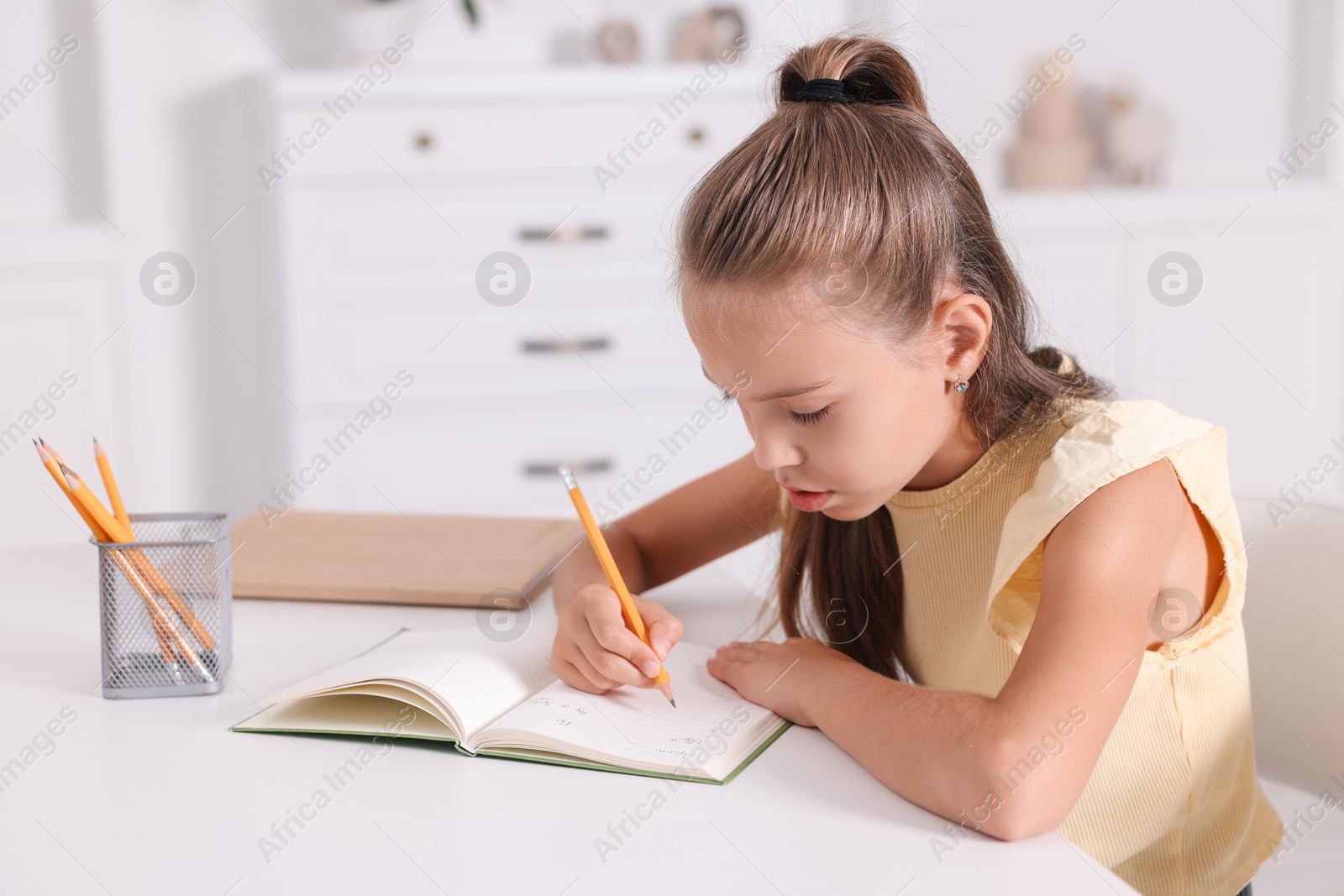 Photo of Girl with incorrect posture doing homework at white desk indoors