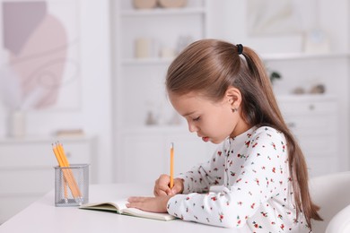 Photo of Girl with correct posture doing homework at white desk indoors