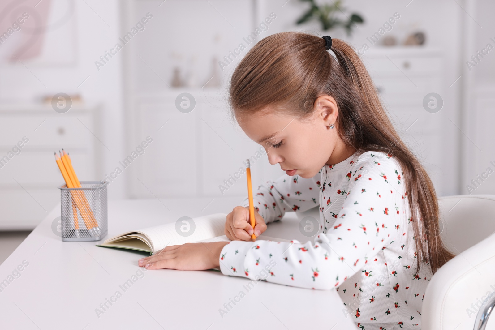 Photo of Girl with incorrect posture doing homework at white desk indoors