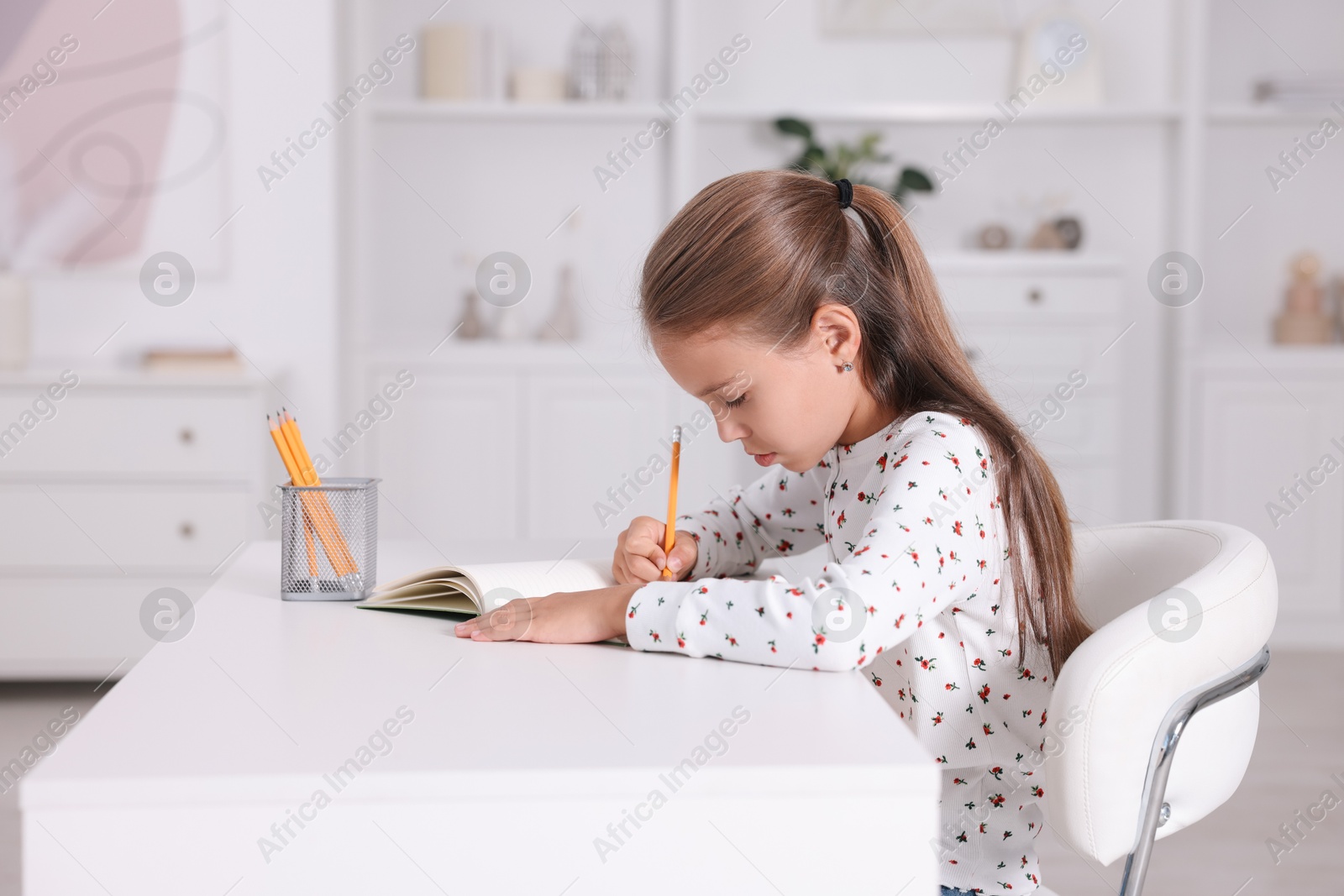 Photo of Girl with incorrect posture doing homework at white desk indoors