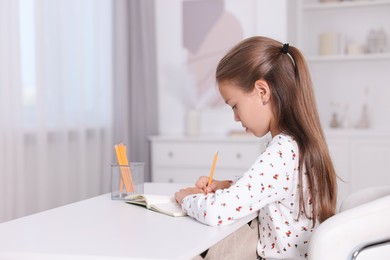 Photo of Girl with correct posture doing homework at white desk indoors