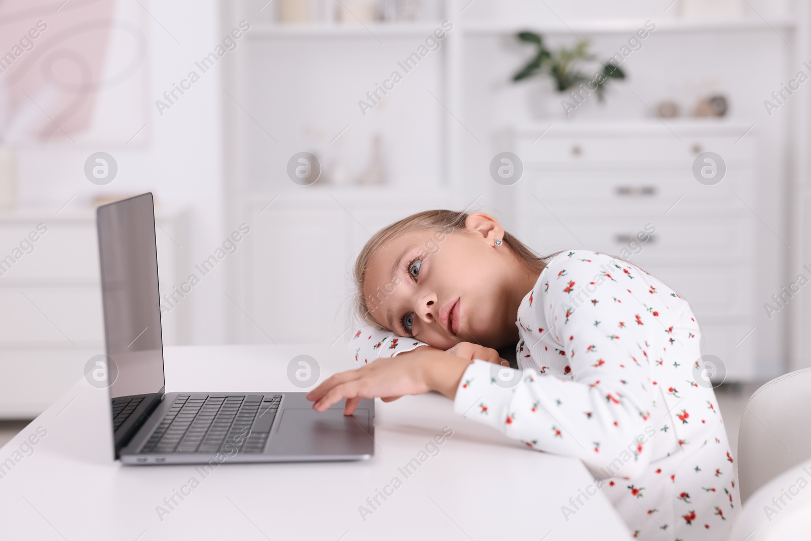 Photo of Girl with incorrect posture using laptop at white desk indoors