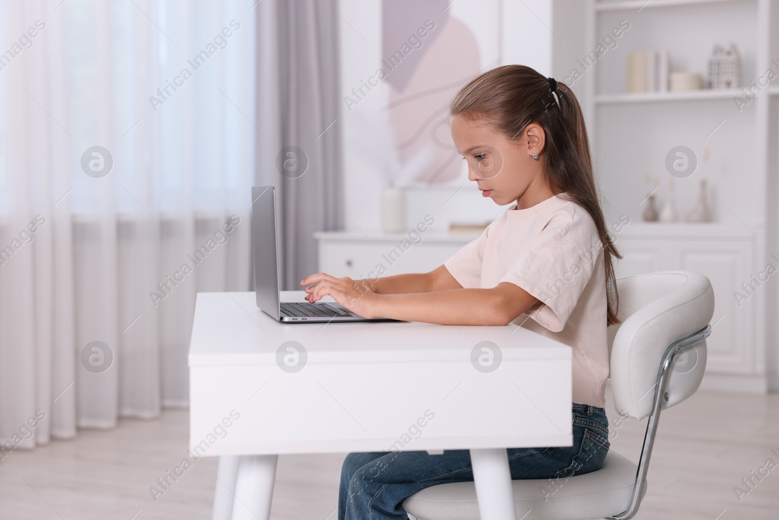 Photo of Girl with correct posture using laptop at white desk indoors