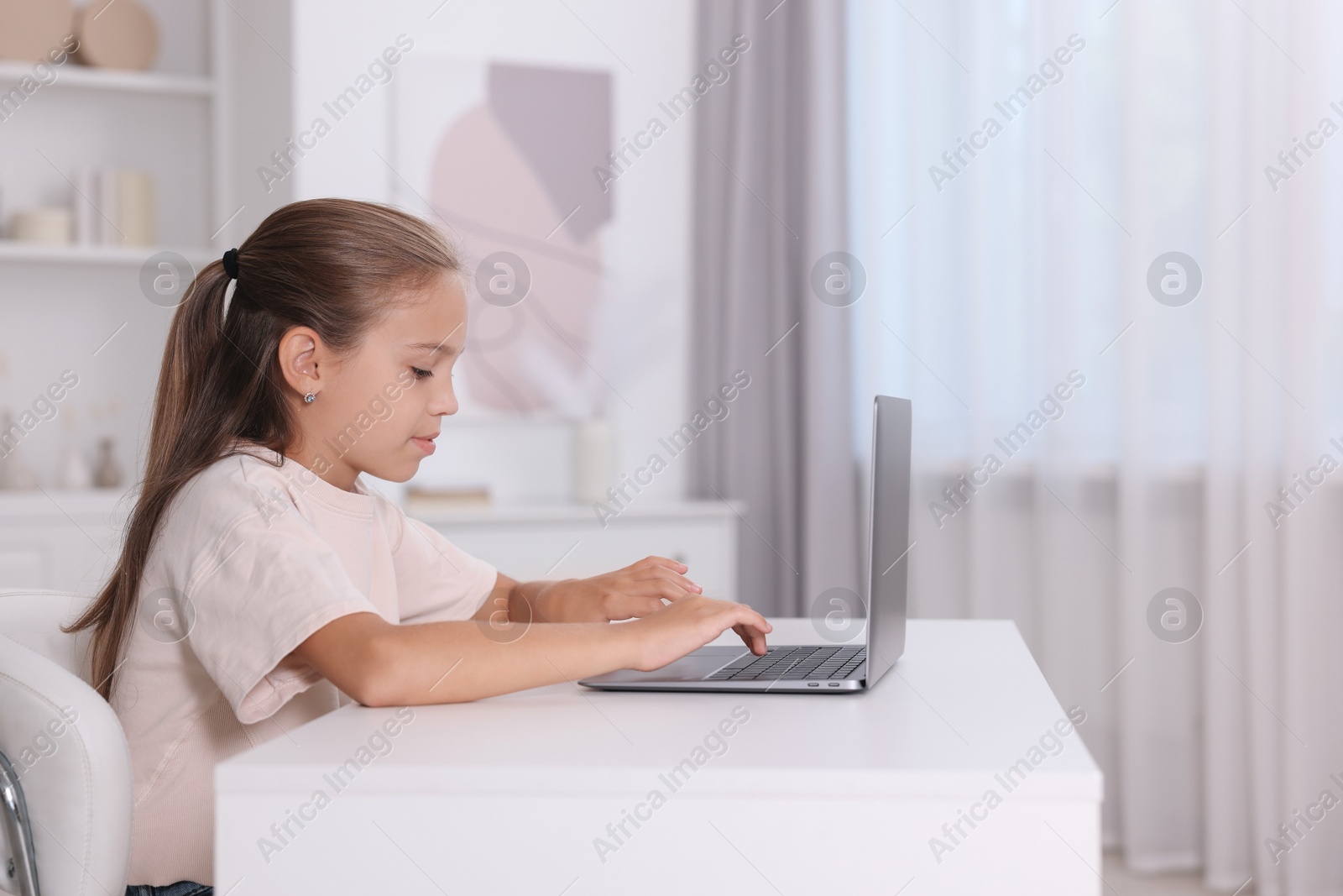 Photo of Girl with incorrect posture using laptop at white desk indoors