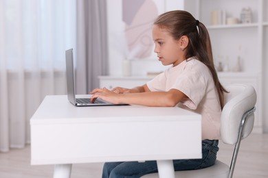 Girl with incorrect posture using laptop at white desk indoors