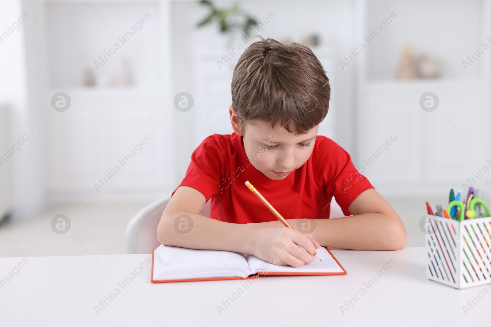 Photo of Boy with incorrect posture doing homework at white desk indoors