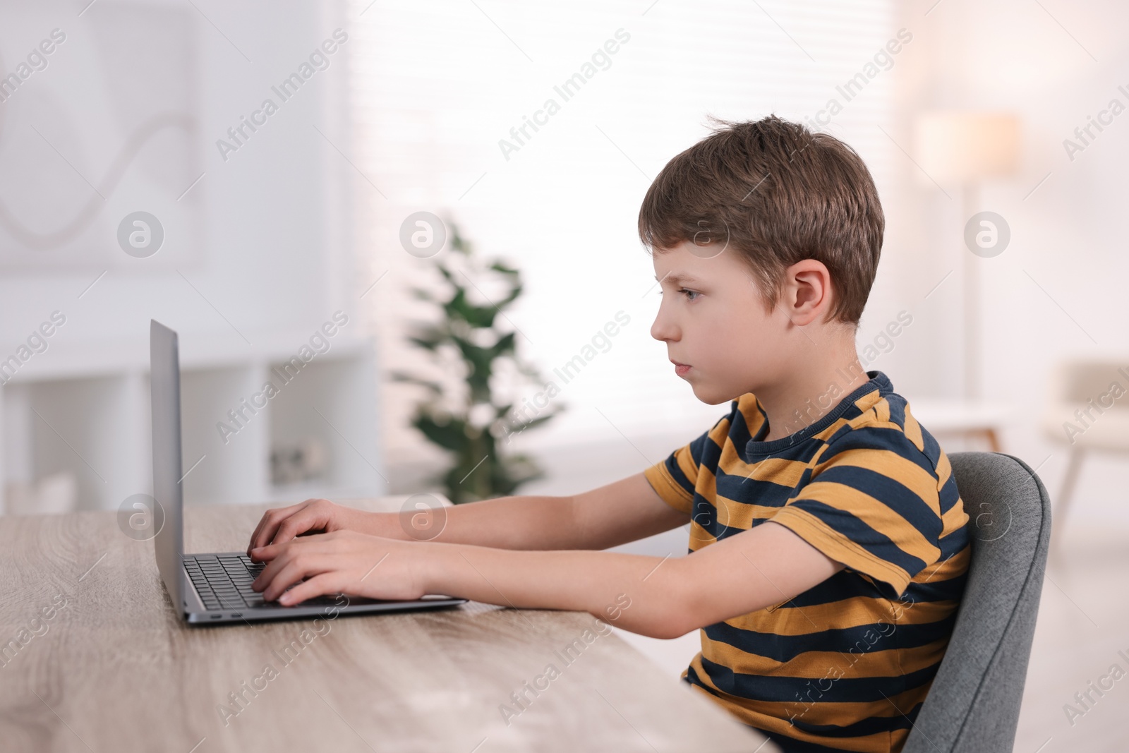 Photo of Boy with incorrect posture using laptop at wooden desk indoors