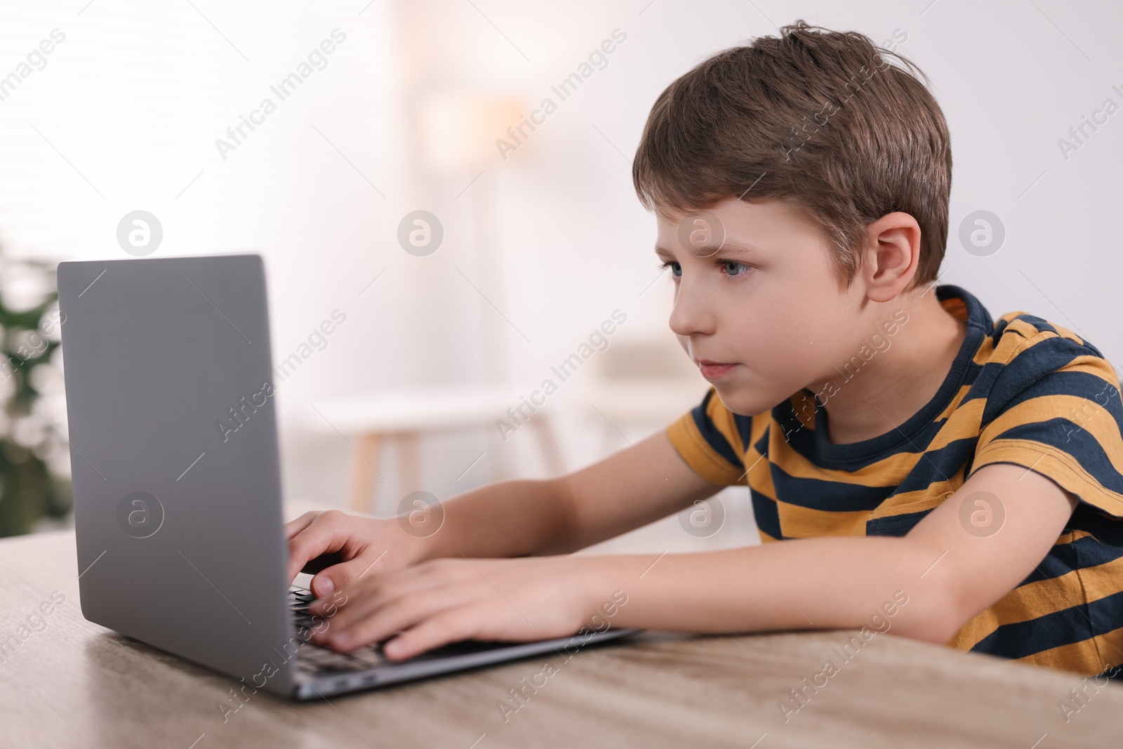 Photo of Boy with incorrect posture using laptop at wooden desk indoors