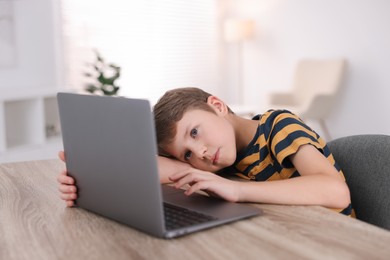 Photo of Boy with incorrect posture using laptop at wooden desk indoors