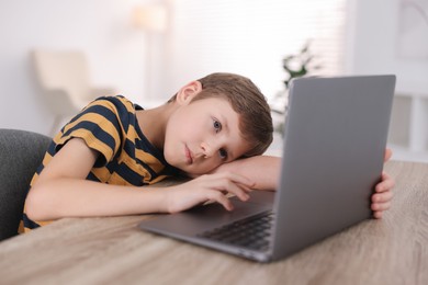 Photo of Boy with incorrect posture using laptop at wooden desk indoors