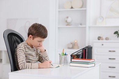 Photo of Boy with incorrect posture doing homework at white desk indoors