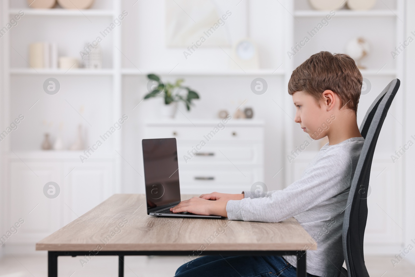 Photo of Boy with correct posture using laptop at wooden desk indoors