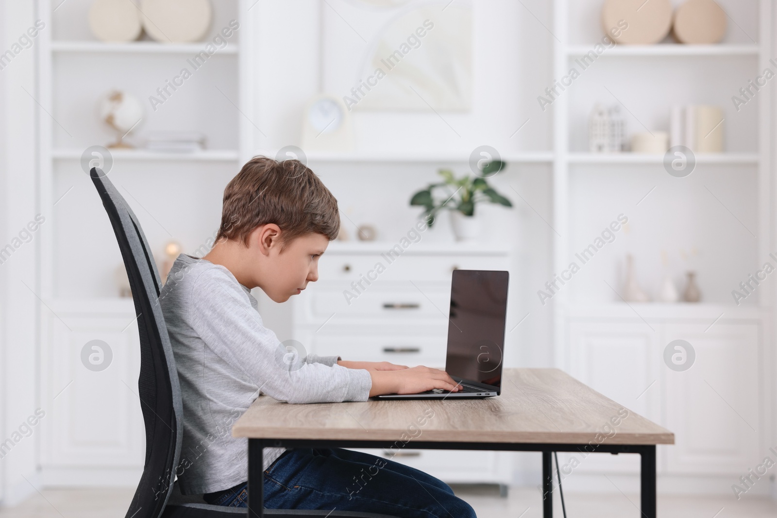 Photo of Boy with incorrect posture using laptop at wooden desk indoors