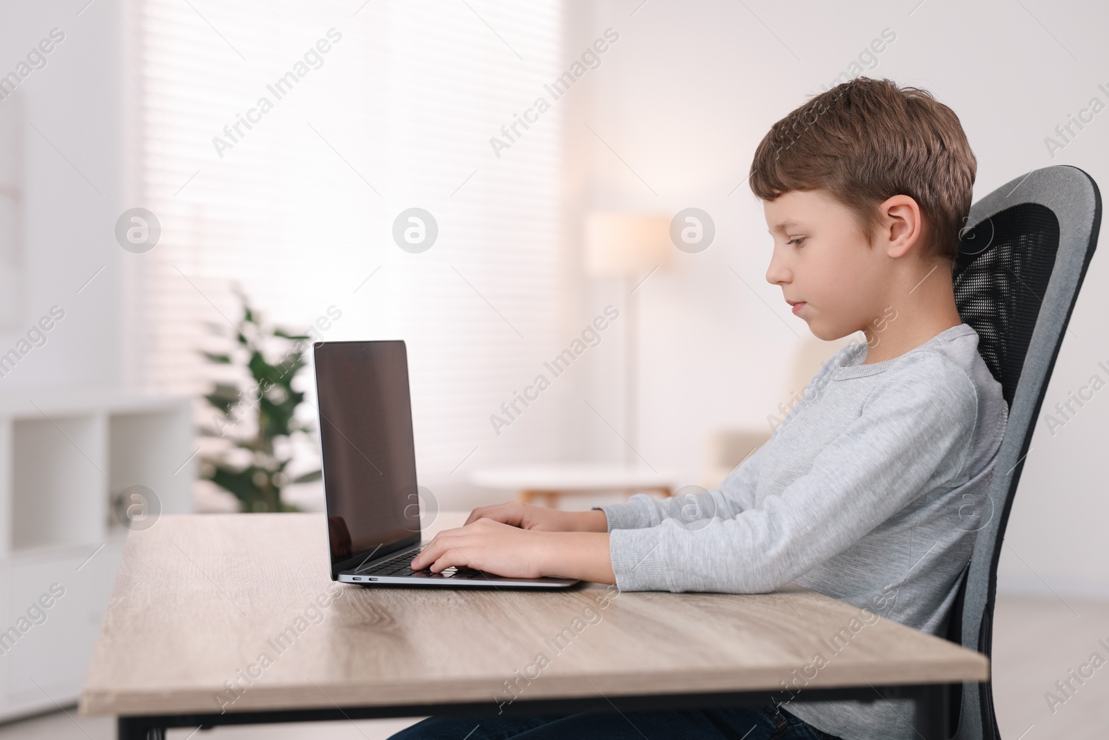 Photo of Boy with correct posture using laptop at wooden desk indoors