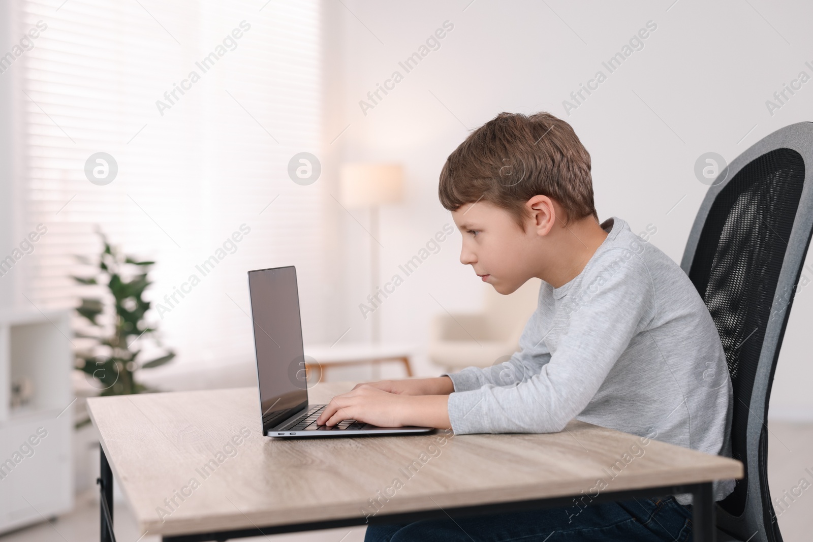 Photo of Boy with incorrect posture using laptop at wooden desk indoors