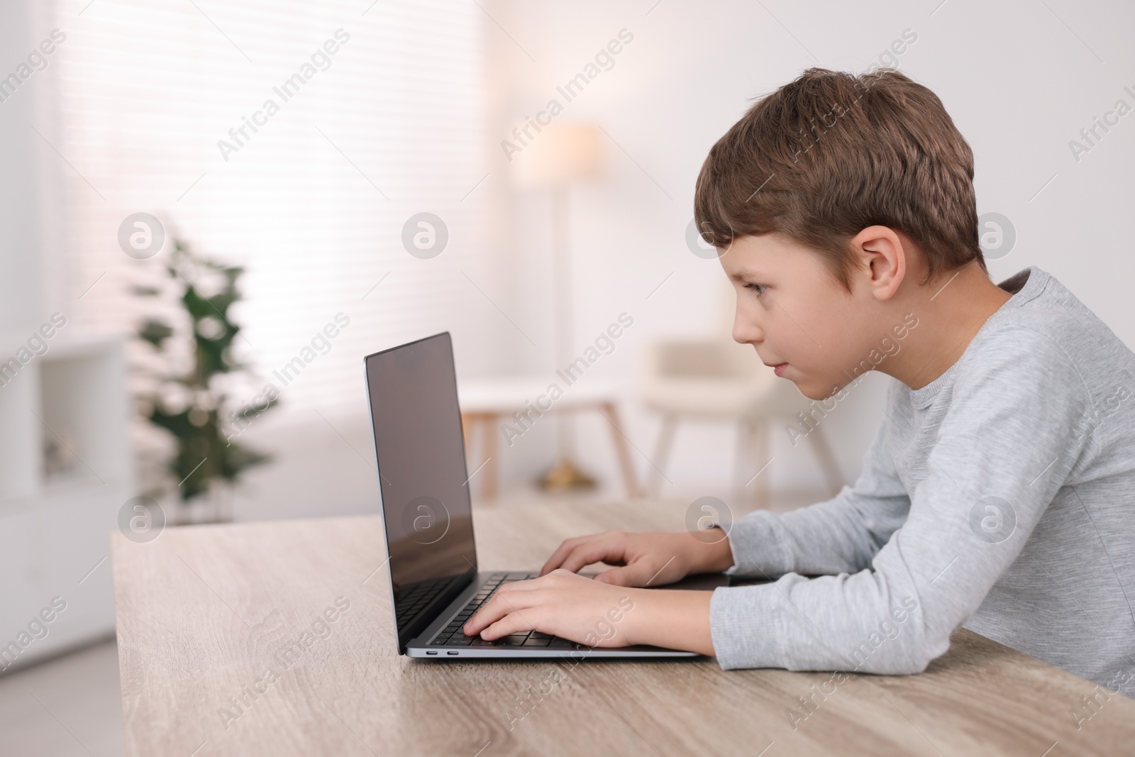 Photo of Boy with incorrect posture using laptop at wooden desk indoors