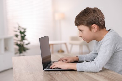 Photo of Boy with incorrect posture using laptop at wooden desk indoors